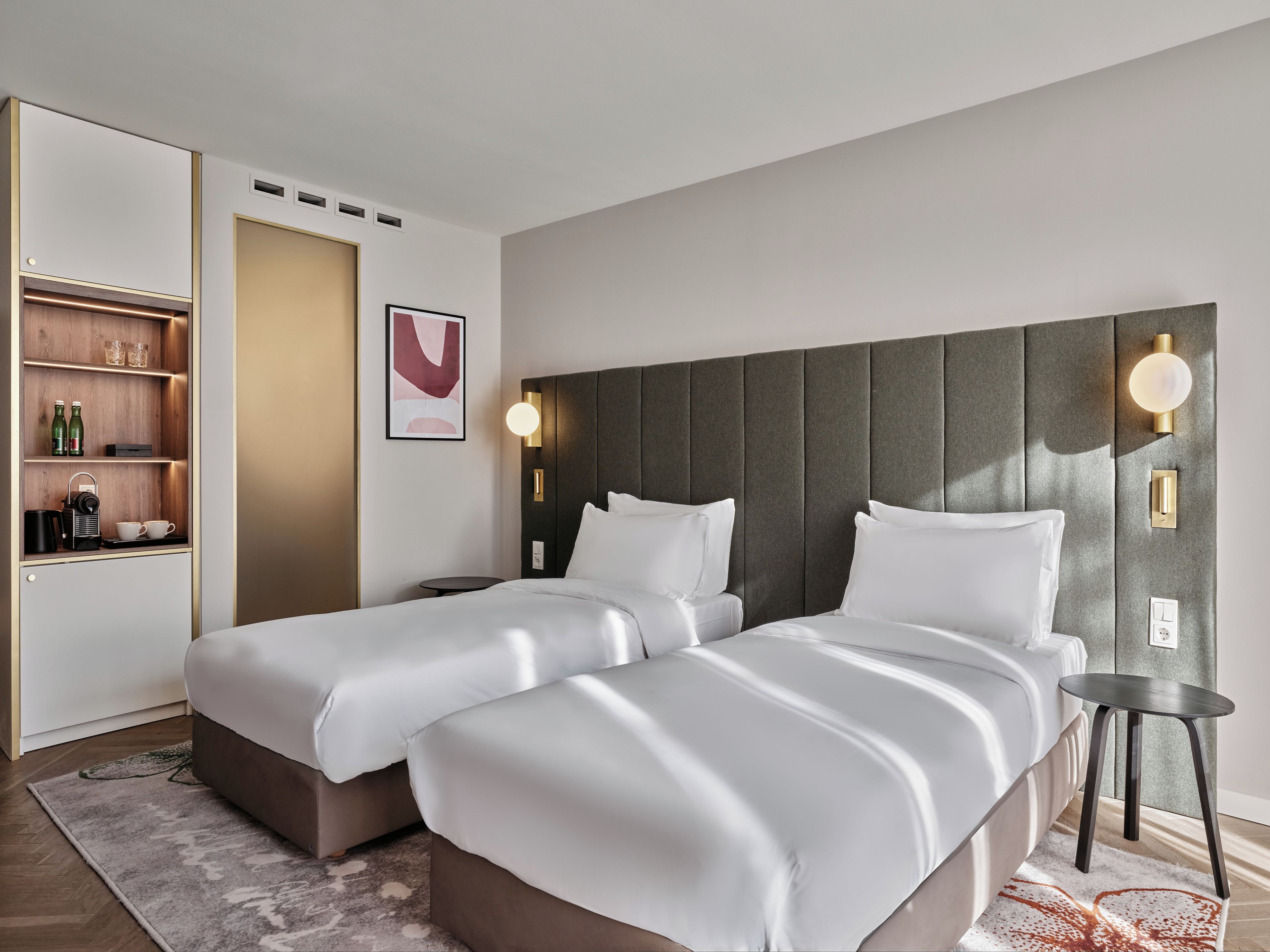 A hotel room with two beds, a minibar, a wall-mounted light fixture, and a framed artwork.