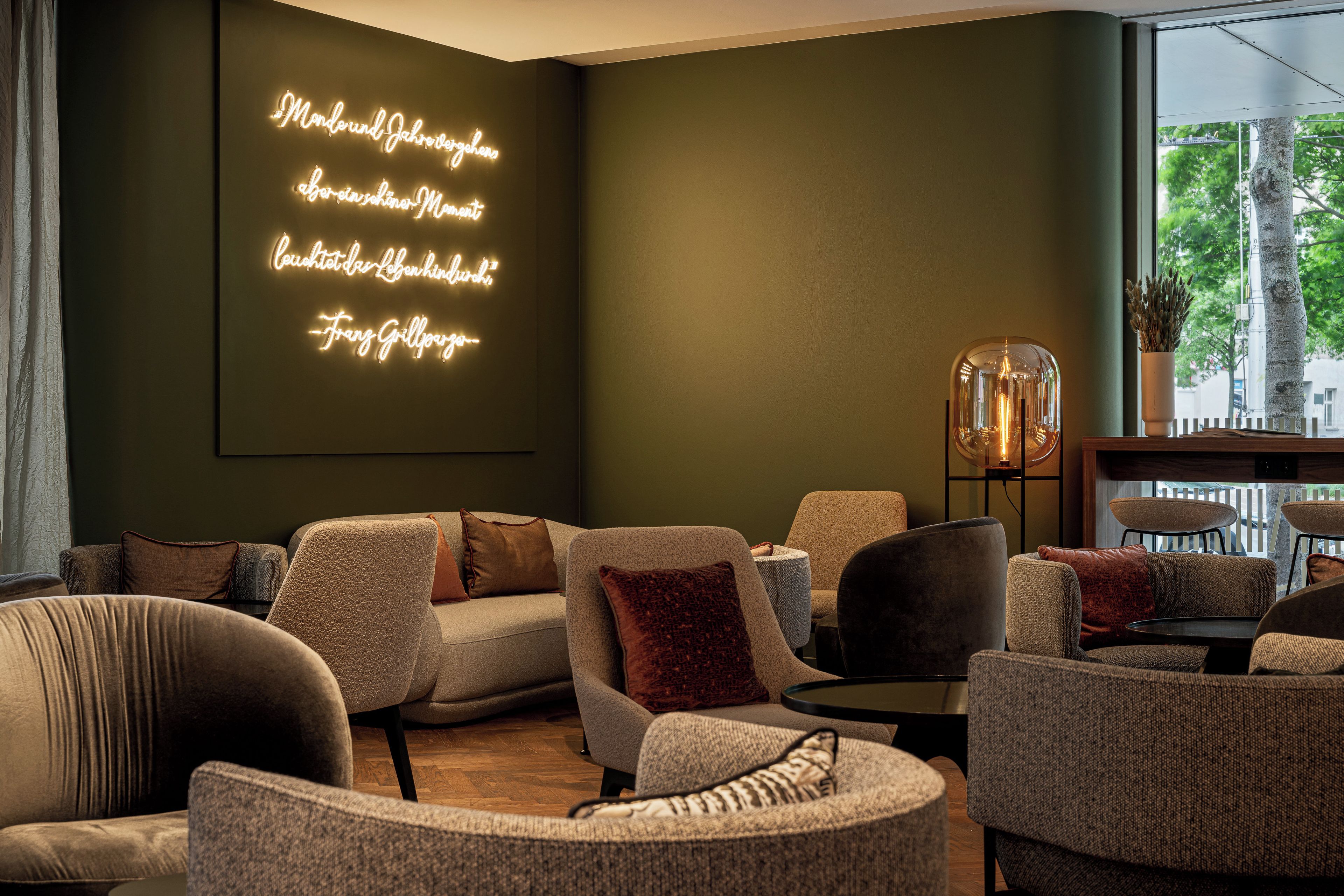 Een moderne woonkamer met een donkergroene wand, een neonbord en diverse zithoeken.
