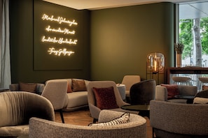 Sala de estar moderna com parede verde escuro, letreiro neon e diversas opções de assentos.