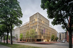 A modern building with a grid-like facade, surrounded by trees and a street with moving vehicles. - Crowne Plaza Vienna by IHG (Vienna)