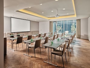 Un salón de conferencias con una pantalla grande, varias mesas, sillas y un proyector.