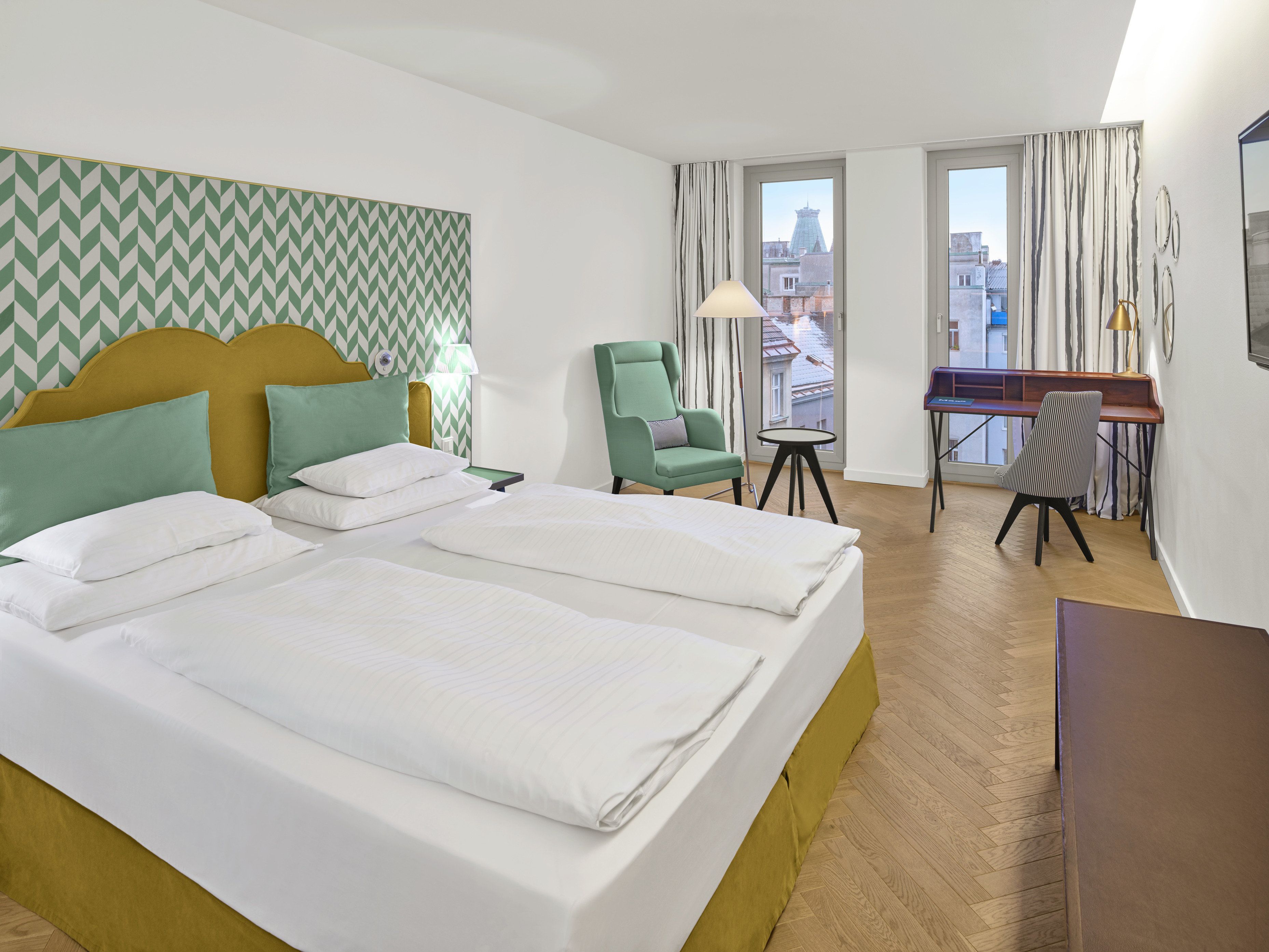 A hotel room with a bed, two chairs, a desk, and a view of the city.