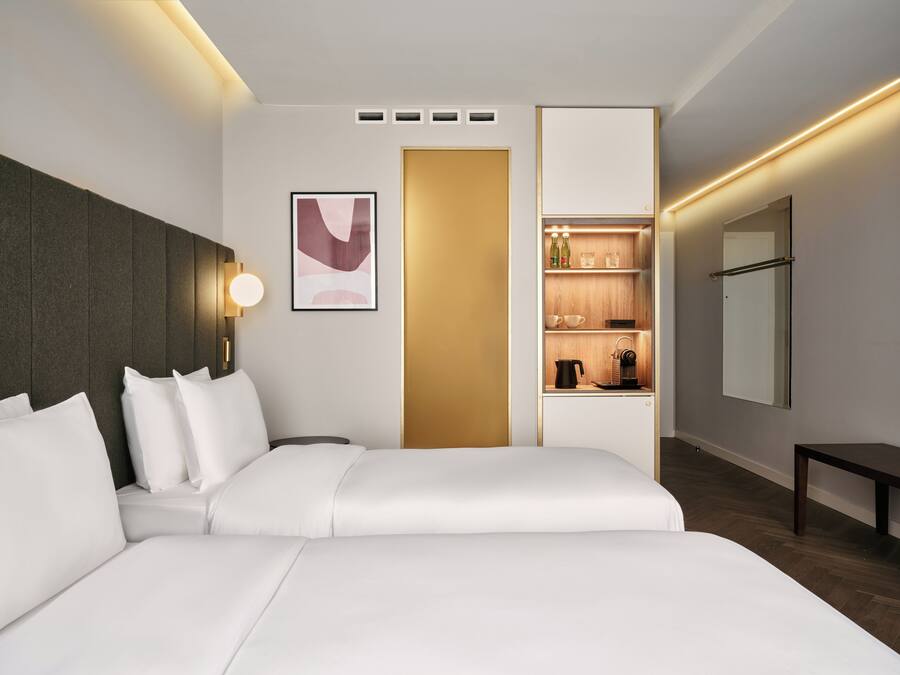 Una habitación de hotel moderna con una cama grande, una mesita de noche, un estante en la pared con artículos de aseo y un espejo.