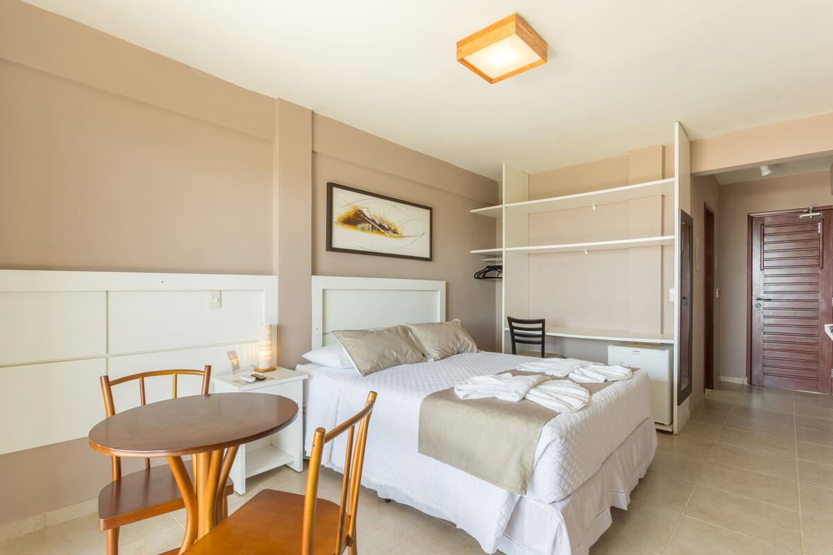 Ein Hotelzimmer mit Bett, Schreibtisch, Stuhl, Nachttisch, Kleiderschrank und einem Bild an der Wand.