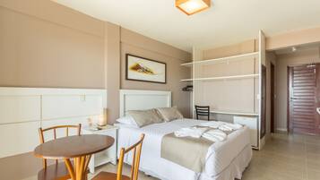 Habitación de hotel con cama, escritorio, silla, mesita de noche, armario y un cuadro en la pared.