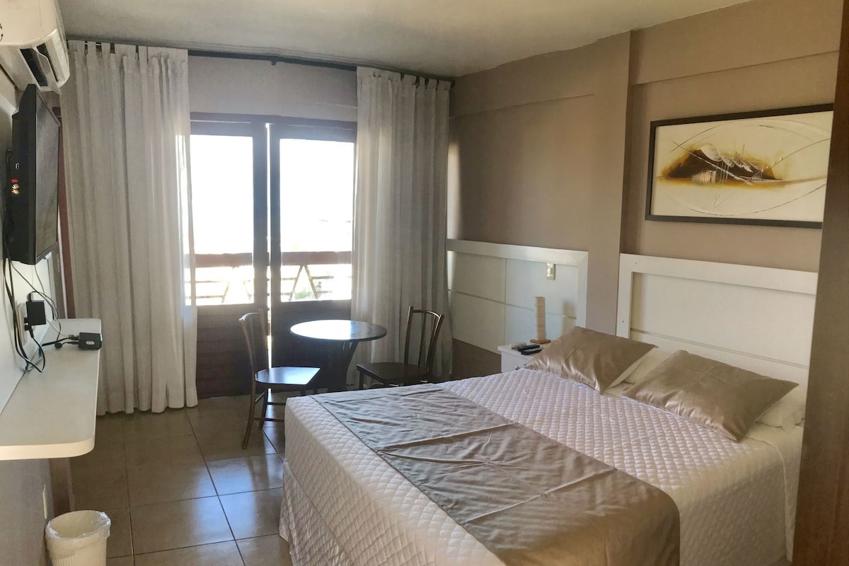 Habitación de hotel con cama, escritorio, silla, mesita y ventana con cortinas.