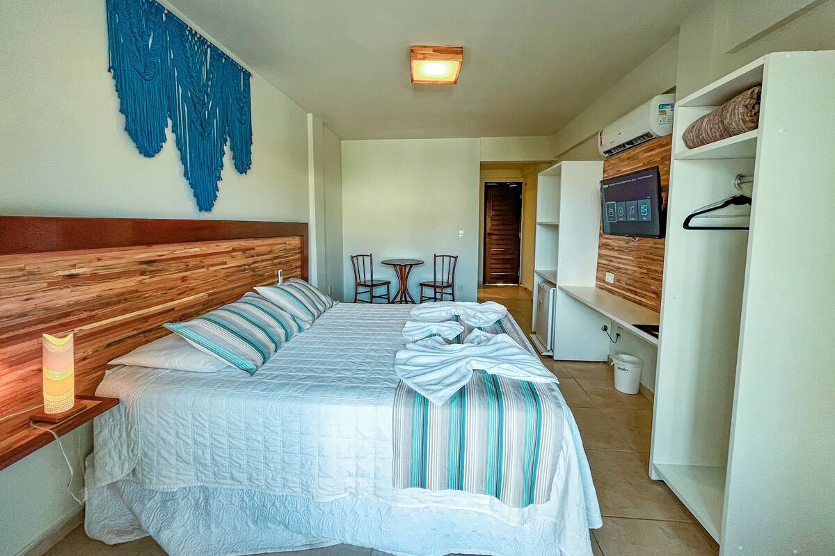Ein Hotelzimmer mit einem großen Bett, einem Holz-Kopfteil, einem an der Wand montierten Fernseher, einem kleinen Tisch mit Stühlen und einem Kleiderschrank.