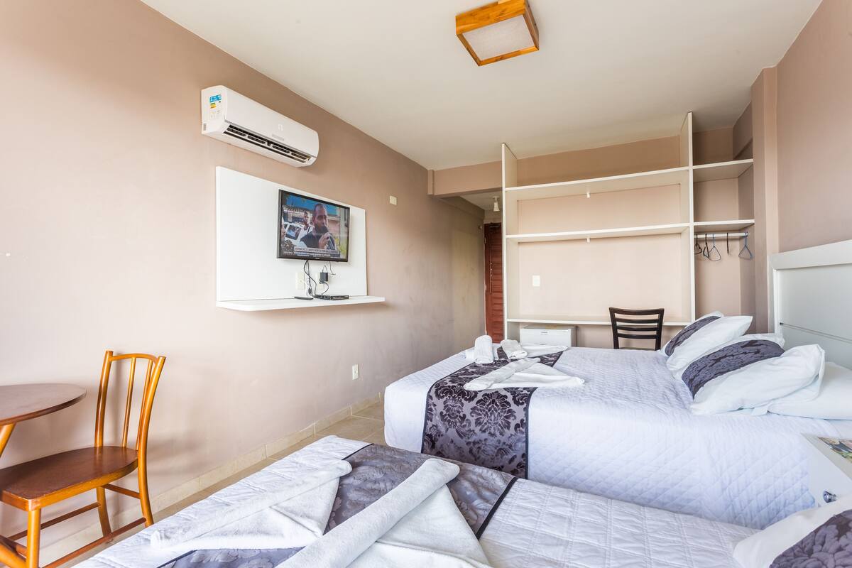 Ein Hotelzimmer mit zwei Betten, einem Schreibtisch, einem Stuhl und einem an der Wand befestigten Fernseher.