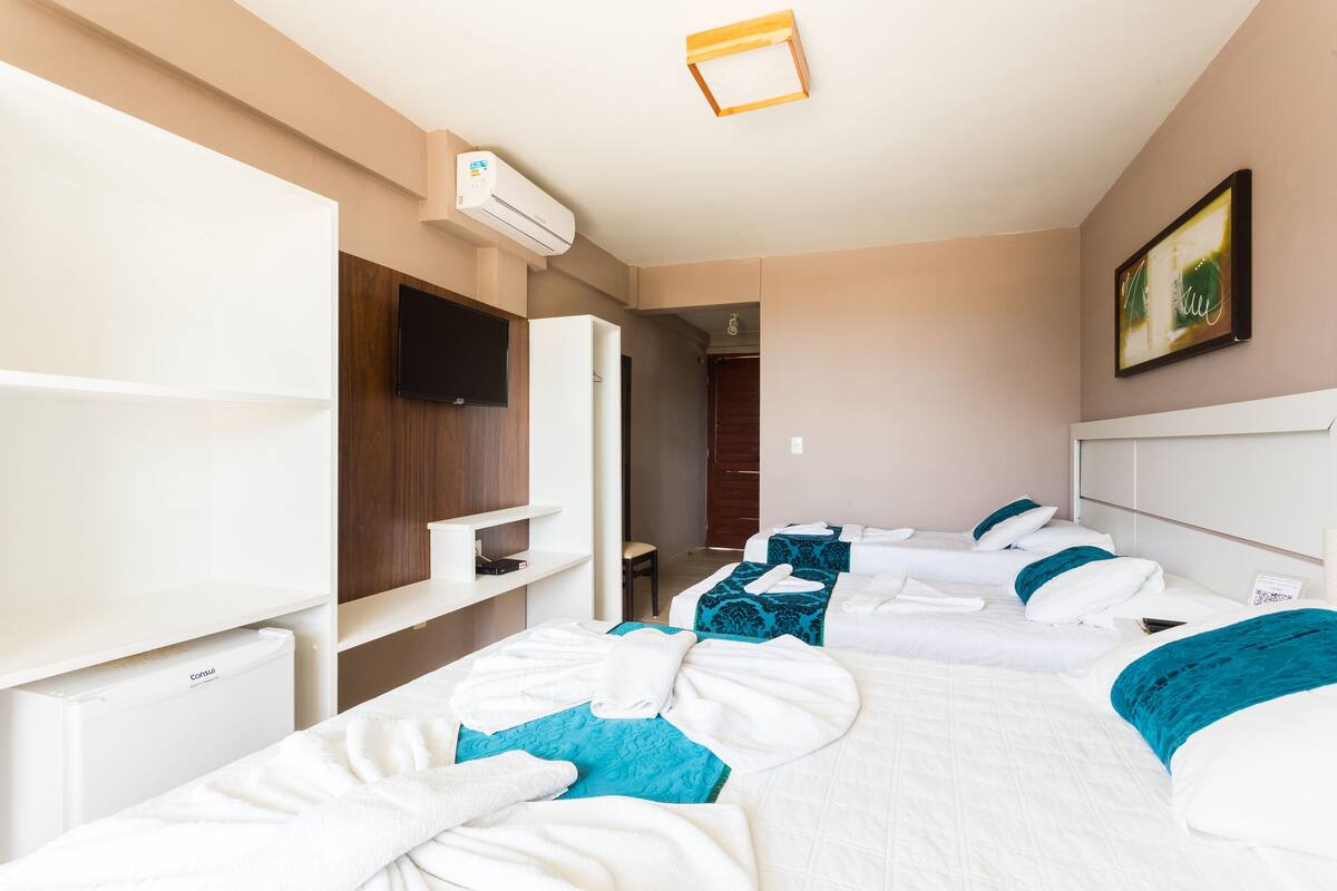 Ein Hotelzimmer mit vier Betten, einem Flachbildfernseher, einer Minibar und einem Deckenventilator.