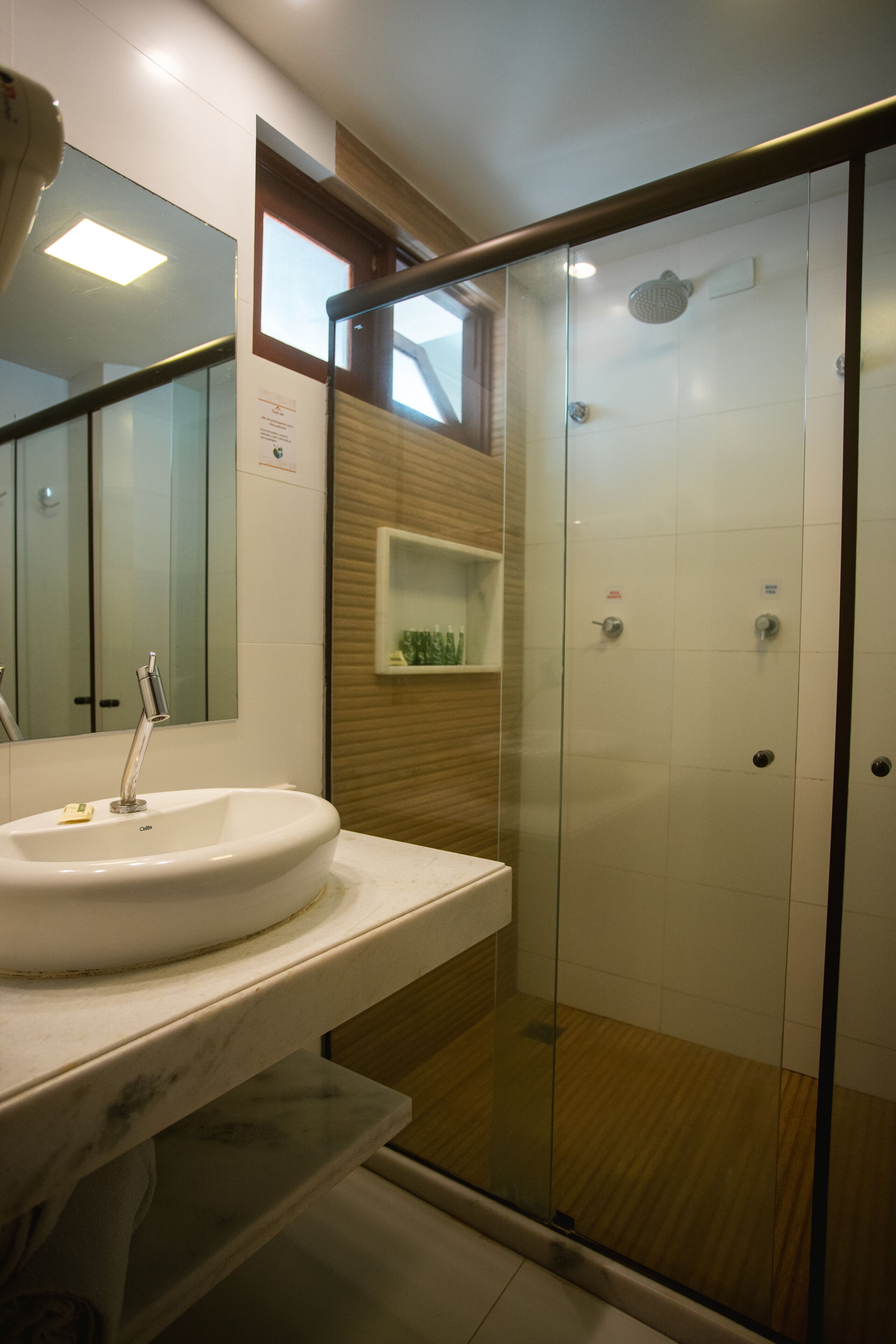 Ein modernes Badezimmer mit einer in Glas abgeschirmten Dusche, einem weißen Waschbecken und einem Holzregal.