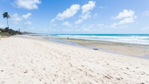 Ein weiter Sandstrand mit Meereswellen, blauem Himmel und einigen Palmen.