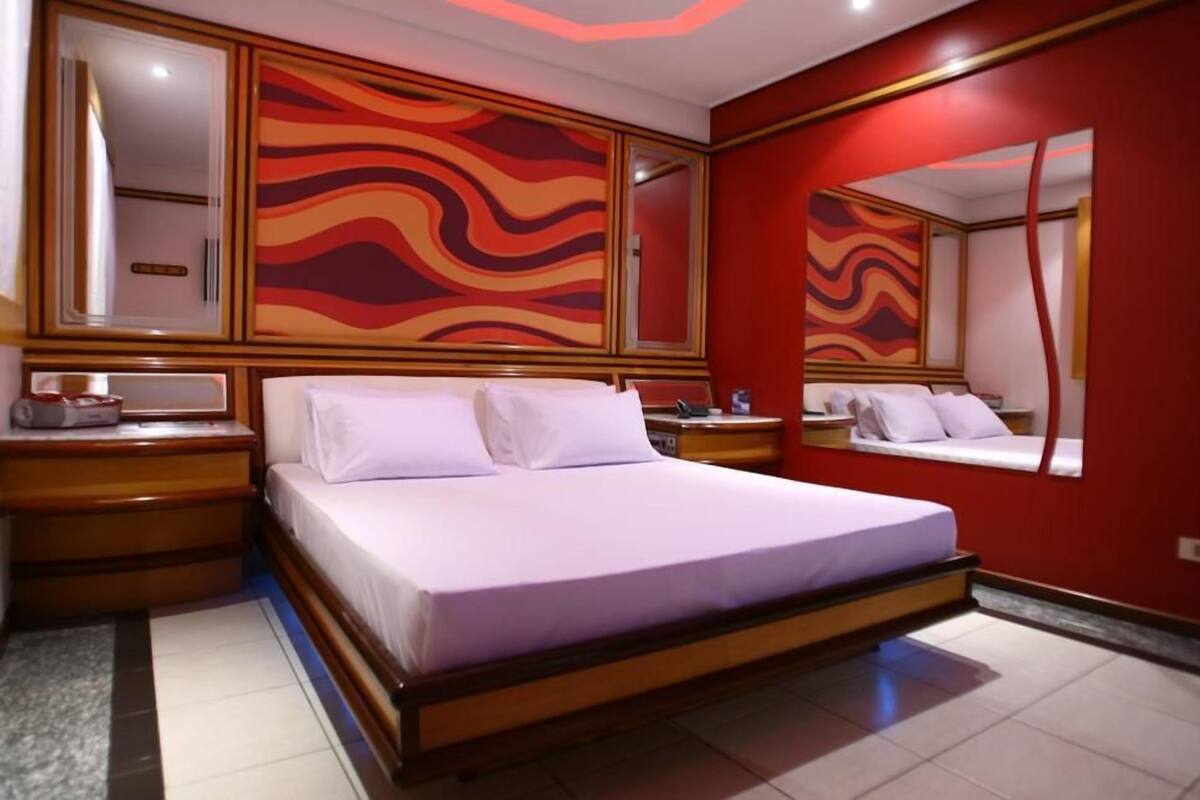 A large bed with a wooden frame, two bedside tables, and a mirror above the bed.