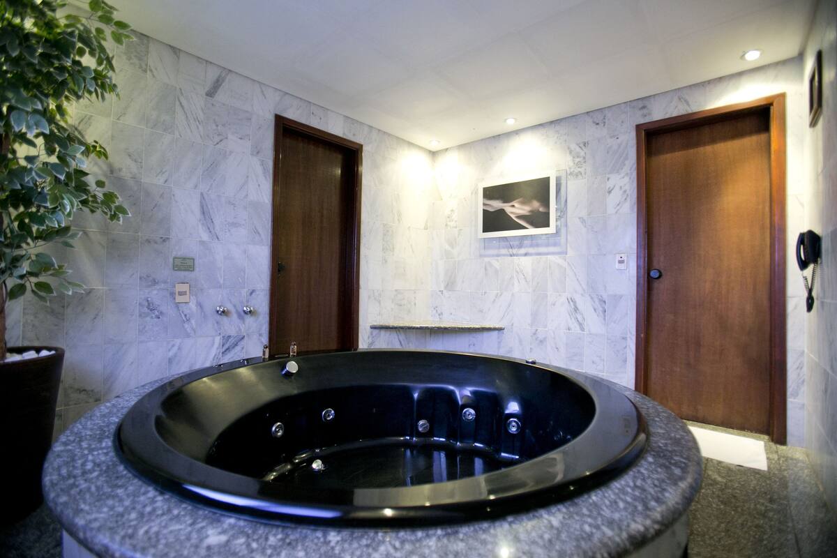 A bathroom with a marble wall, a large black bathtub, wooden doors, and a potted plant.