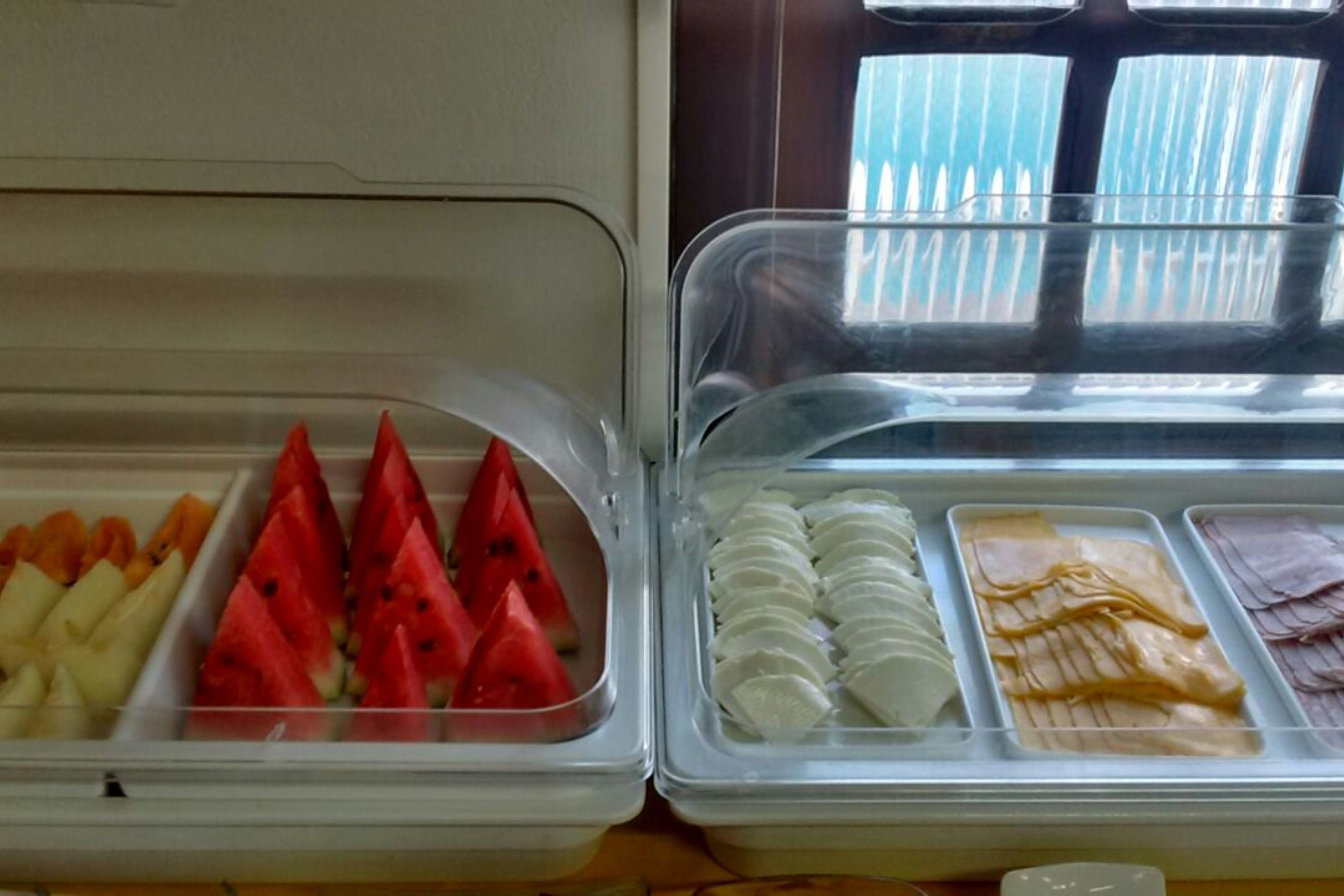 Una vetrina refrigerata con diversi prodotti alimentari, tra cui frutta a fette e salumi.