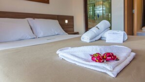 A neatly made bed with white linens and a rolled towel, a pair of Lacto wraps on a towel, and a framed picture on the wall. - Hotel Pousada Paradise (Caraguatatuba)