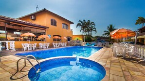 A swimming pool with a tiled deck, surrounded by white chairs and orange umbrellas. - Hotel Pousada Paradise (Caraguatatuba)