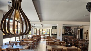 A spacious restaurant with high ceilings and natural light from large windows. Tables are arranged in rows with wooden chairs. - Hotel Pousada Paradise (Caraguatatuba)