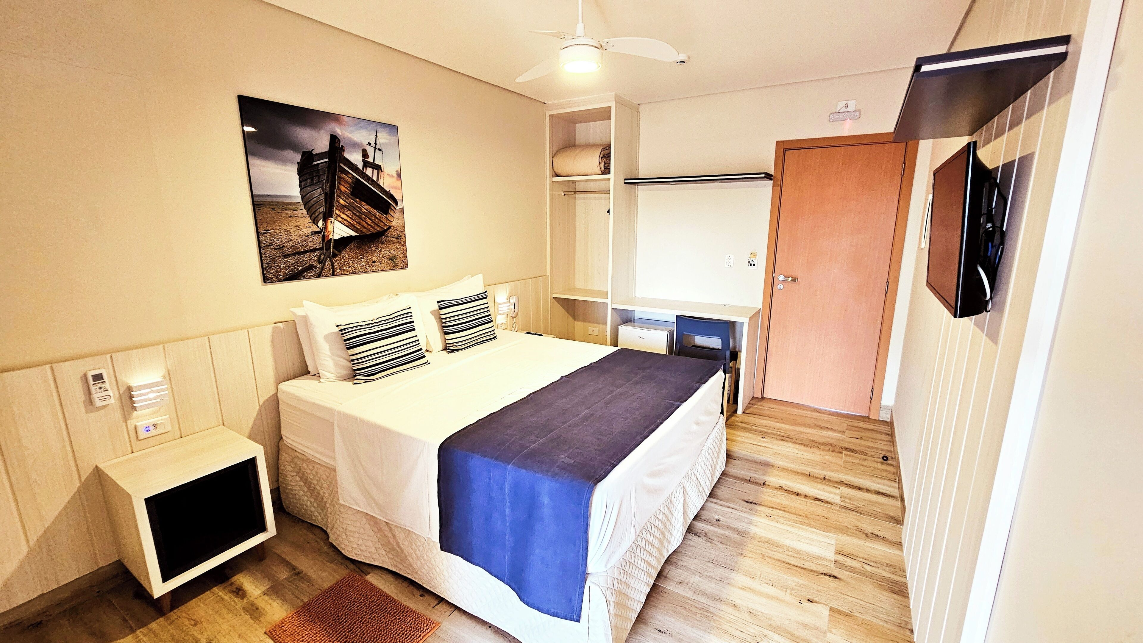 Ein Hotelzimmer mit einem Bett, einem Nachttisch und einem an der Wand befestigten Fernseher.
