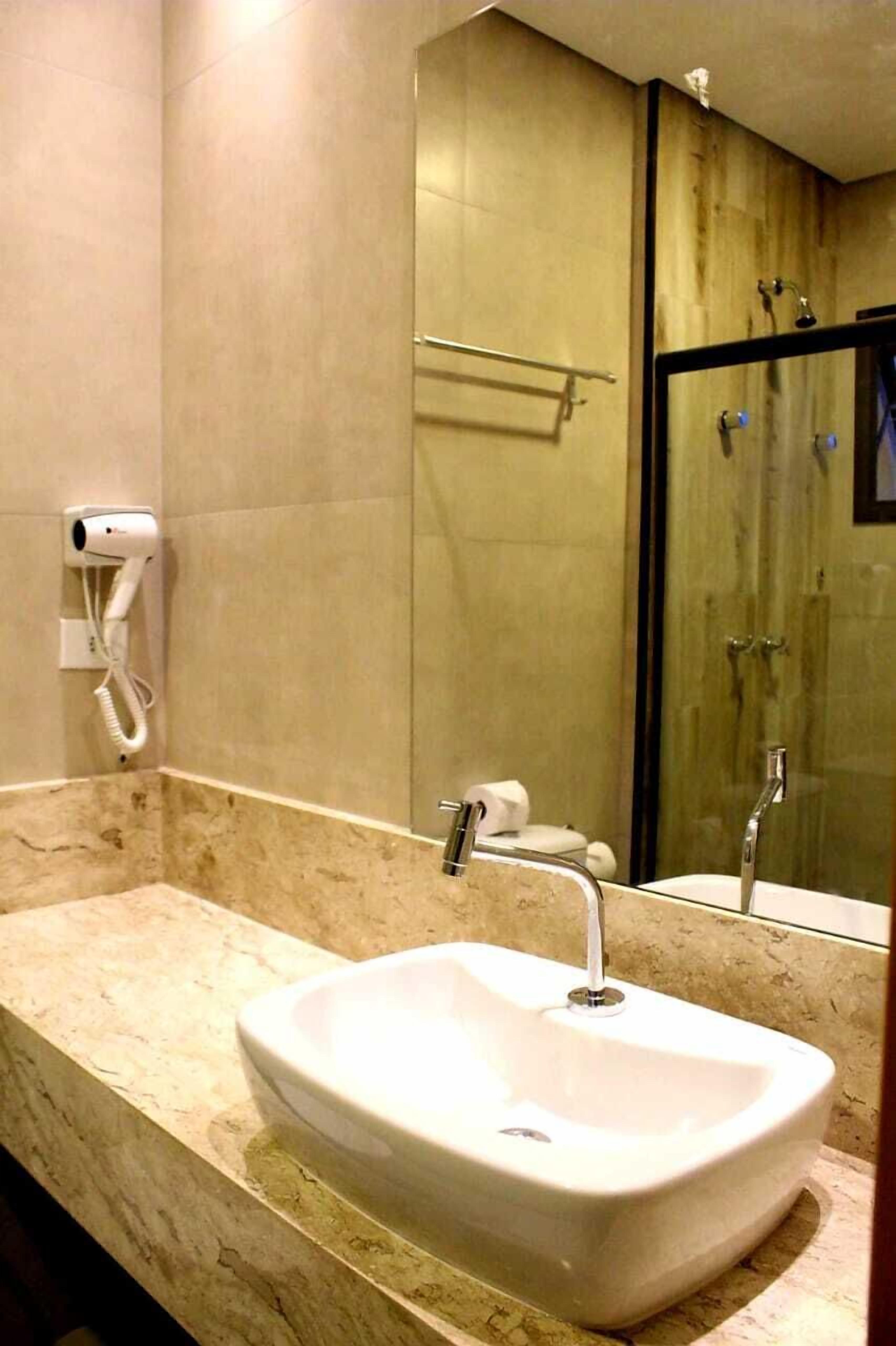 A bathroom with a white sink, a mirror, and a hairdryer on the wall.
