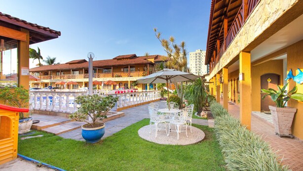 A courtyard with a small lawn, outdoor seating, and a building with balconies. - Hotel Pousada Paradise (Caraguatatuba)