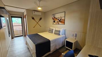 A hotel room with a bed, a desk, a chair, a ceiling fan, and a window.