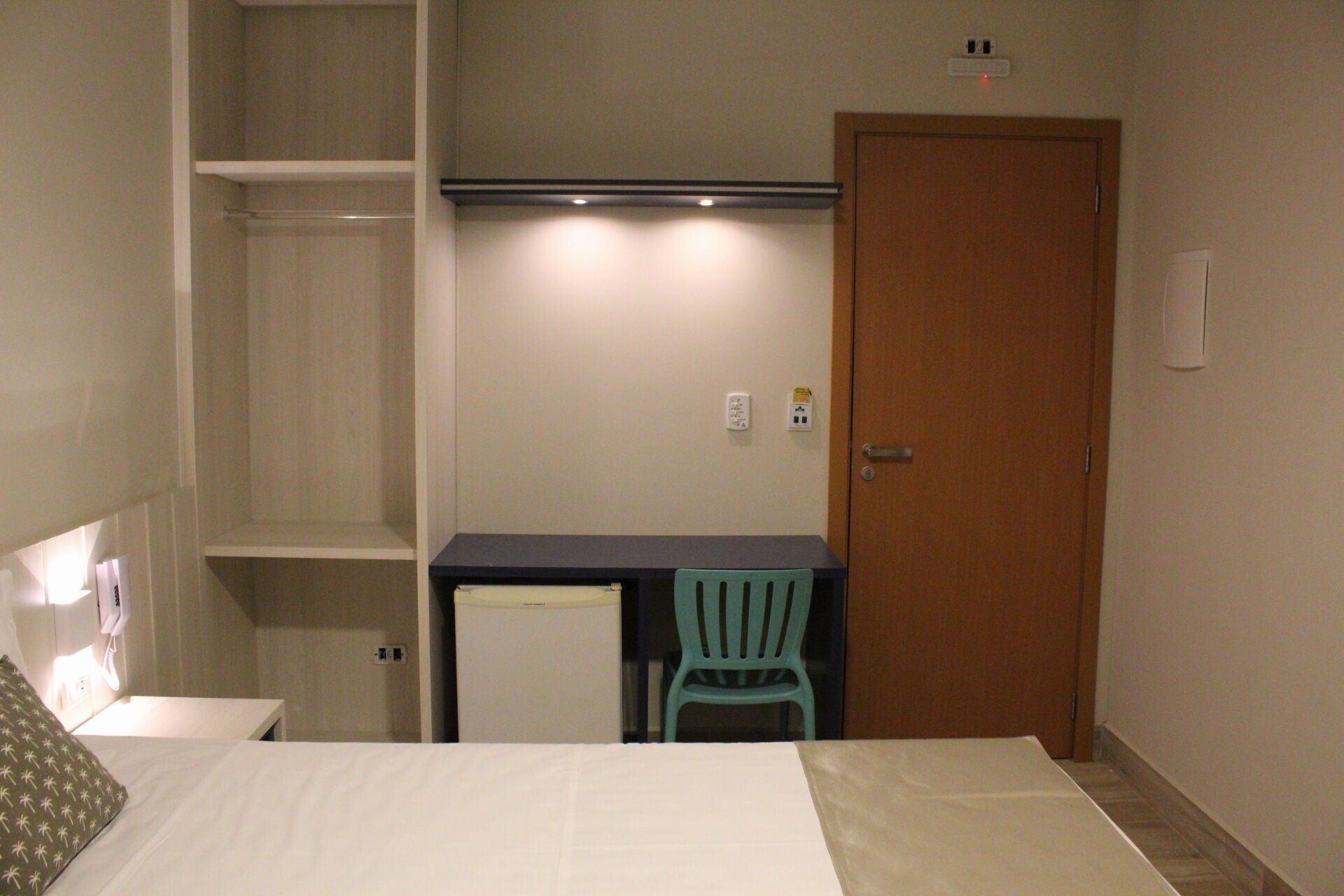 A hotel room with a bed, a desk, a chair, a wardrobe, and a door.