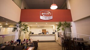 A hotel reception area with a red sign, multiple seating arrangements, and a counter. - Druds Hotel Hortolândia (Hortolandia)