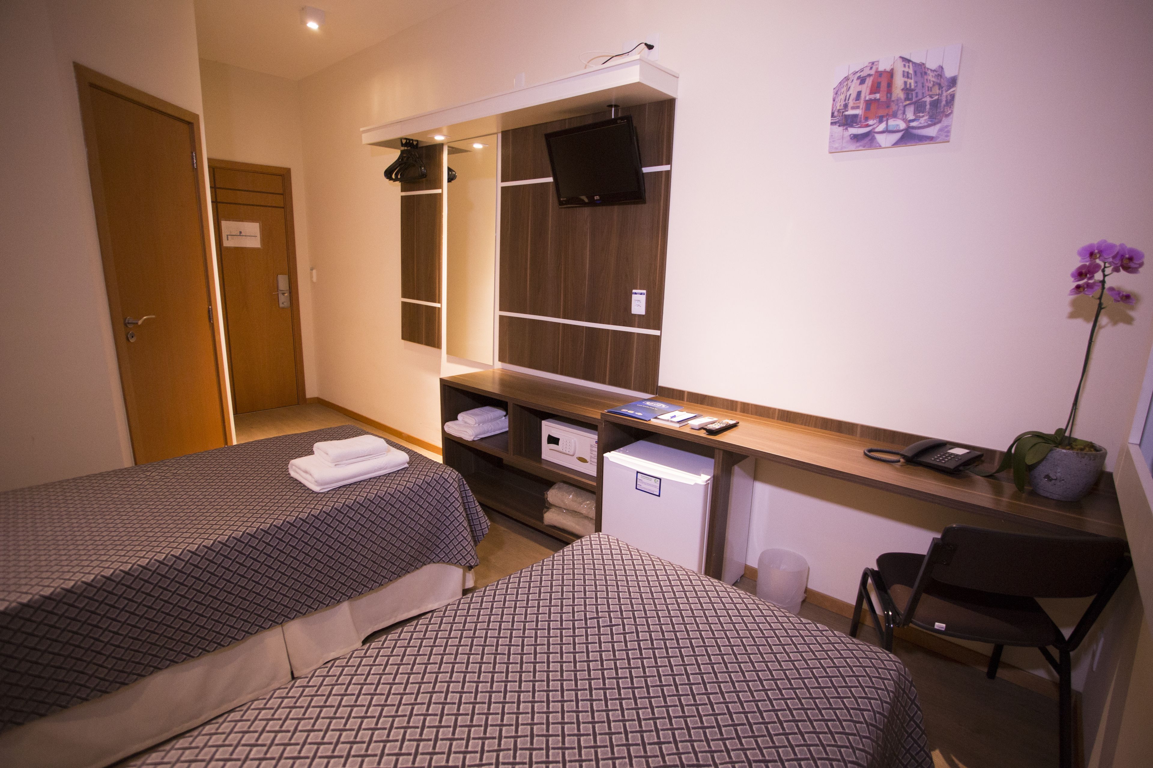 A hotel room with two beds, a desk with a computer, a TV, and a small seating area.