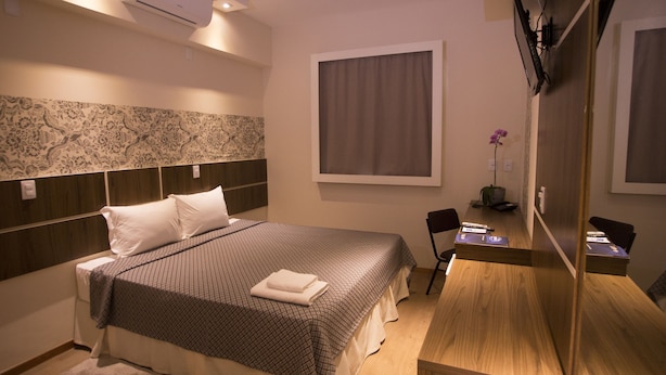 A hotel room with a large bed, a desk, and a mirror. - Druds Hotel Hortolândia (Hortolandia)
