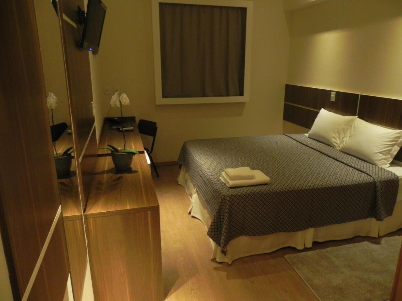 A hotel room with a bed, bedside table, chair, TV, and window.