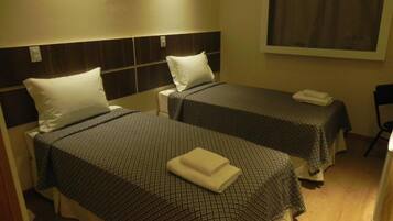 Una habitación de hotel con dos camas individuales, cada una con cabecero y almohada.