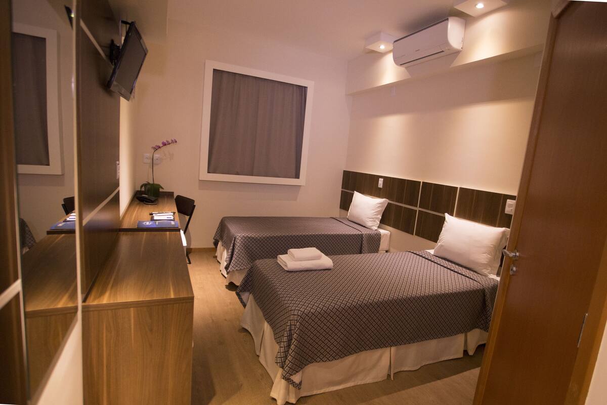 Une chambre d’hôtel avec deux lits, un bureau, une chaise, une télévision et un appareil de climatisation.
