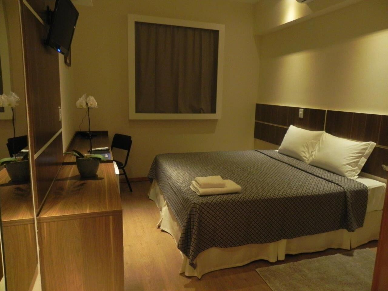 A hotel room with a bed, a desk, a chair, a TV, and a window with curtains.