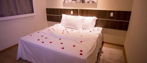 Una cama bien hecha con sábanas blancas y pétalos de rosa, un cabecero de madera y una obra de arte de la Torre Eiffel colgada en la pared.