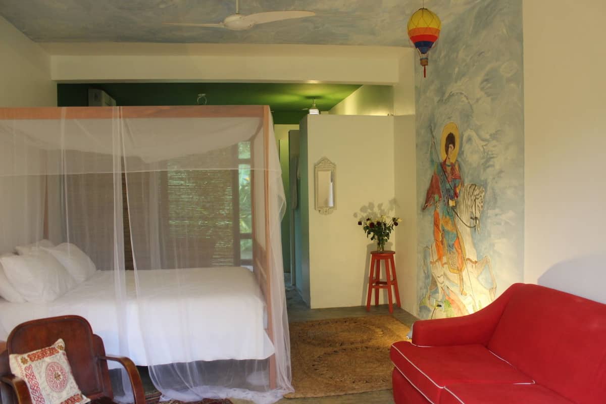 A bedroom with a four-poster bed, a red sofa, and a mural on the wall.