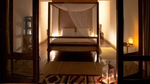 Ein Zimmer mit einem Bett, einem Nachttisch, einer Lampe und Blick durch eine offene Tür.
