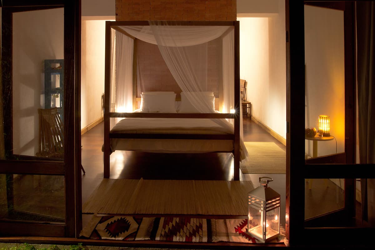 A room with a bed, a bedside table, a lamp, and a view through an open door.