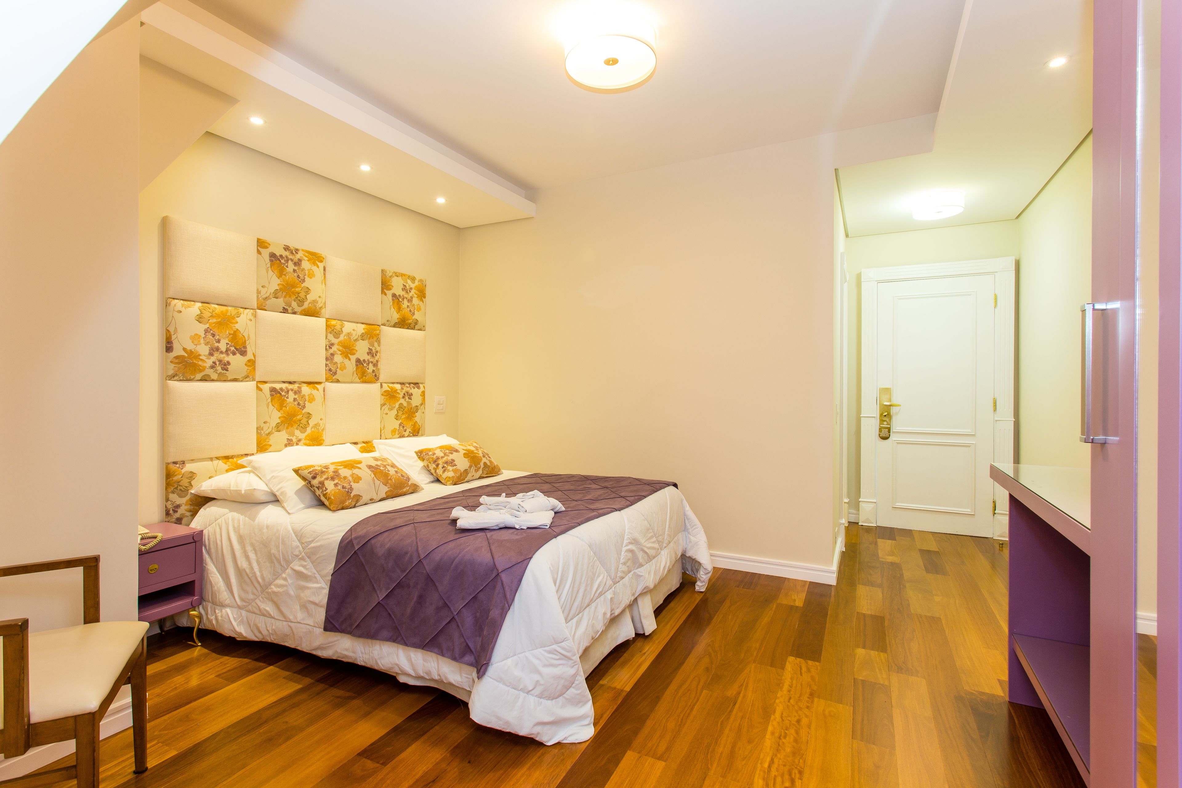Quarto com cama, mesa de cabeceira, cadeira e porta.