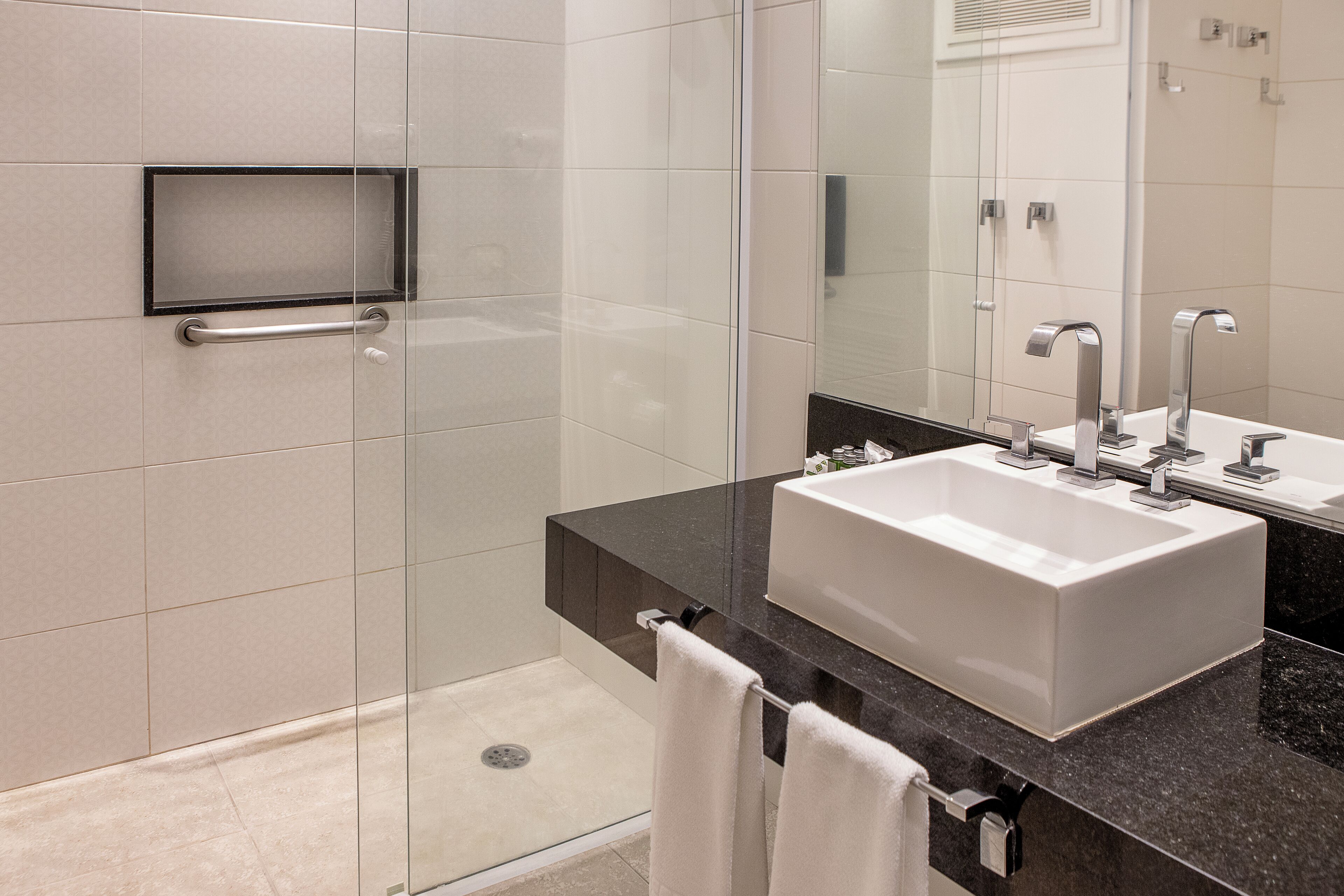 A modern bathroom with a glass shower enclosure, a white sink with two faucets, and a black countertop.