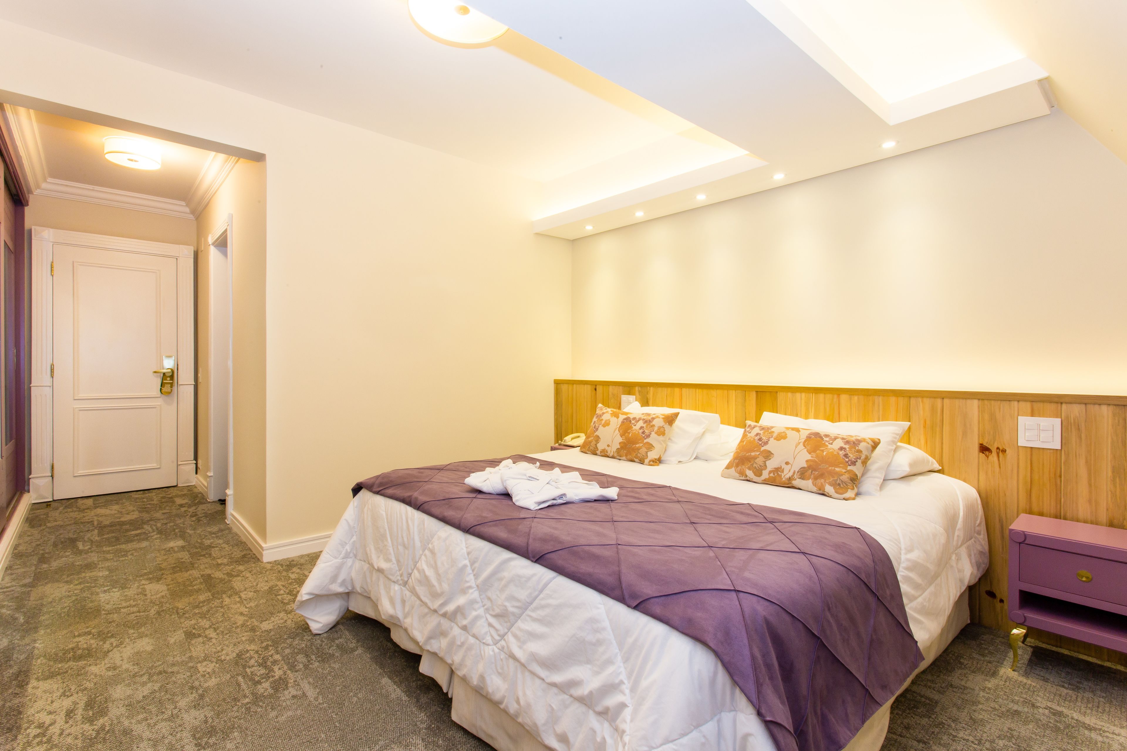 A hotel room with a large bed, a wooden headboard, and a small bedside table.