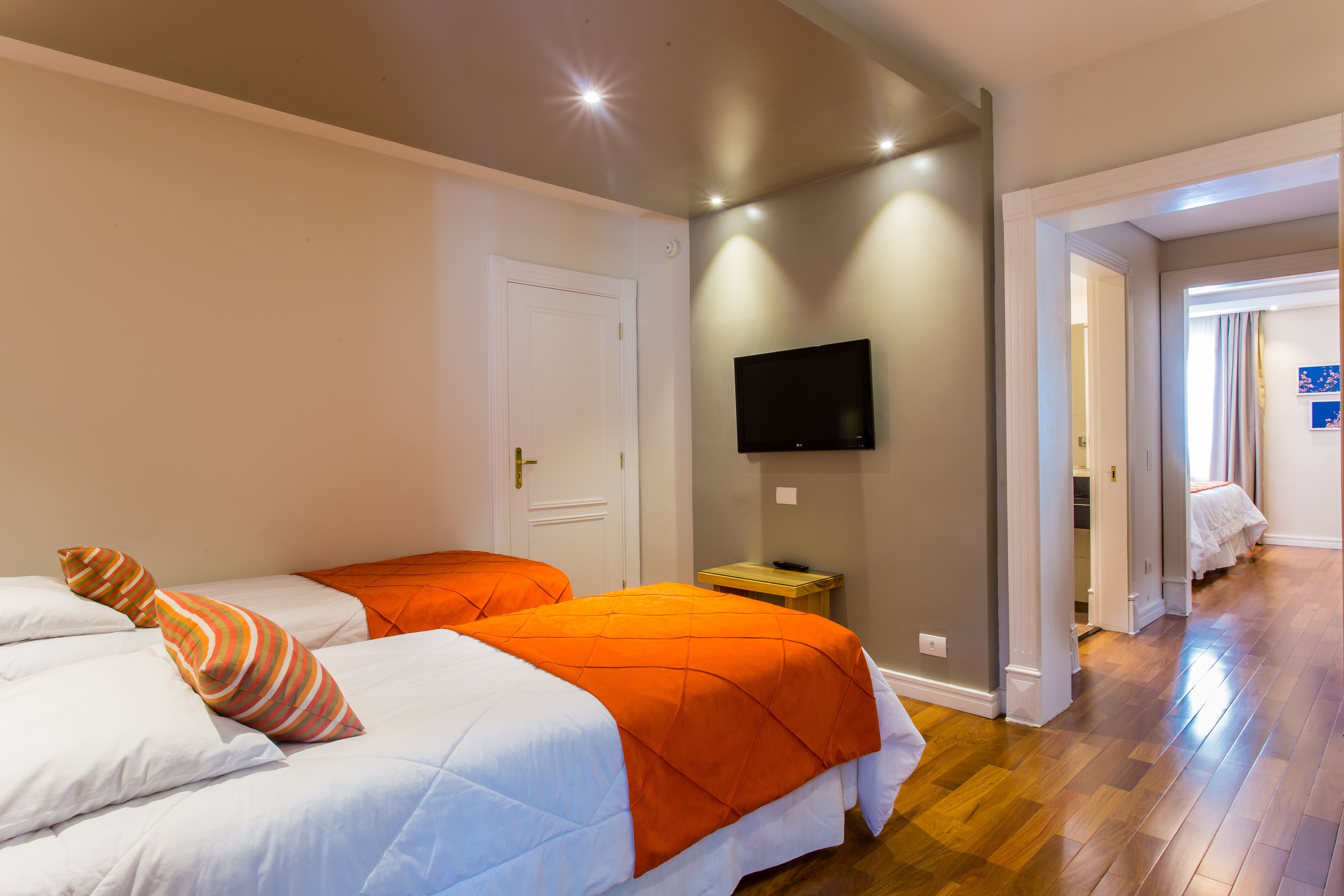 A hotel room with two beds, a TV on the wall, and a wooden floor.