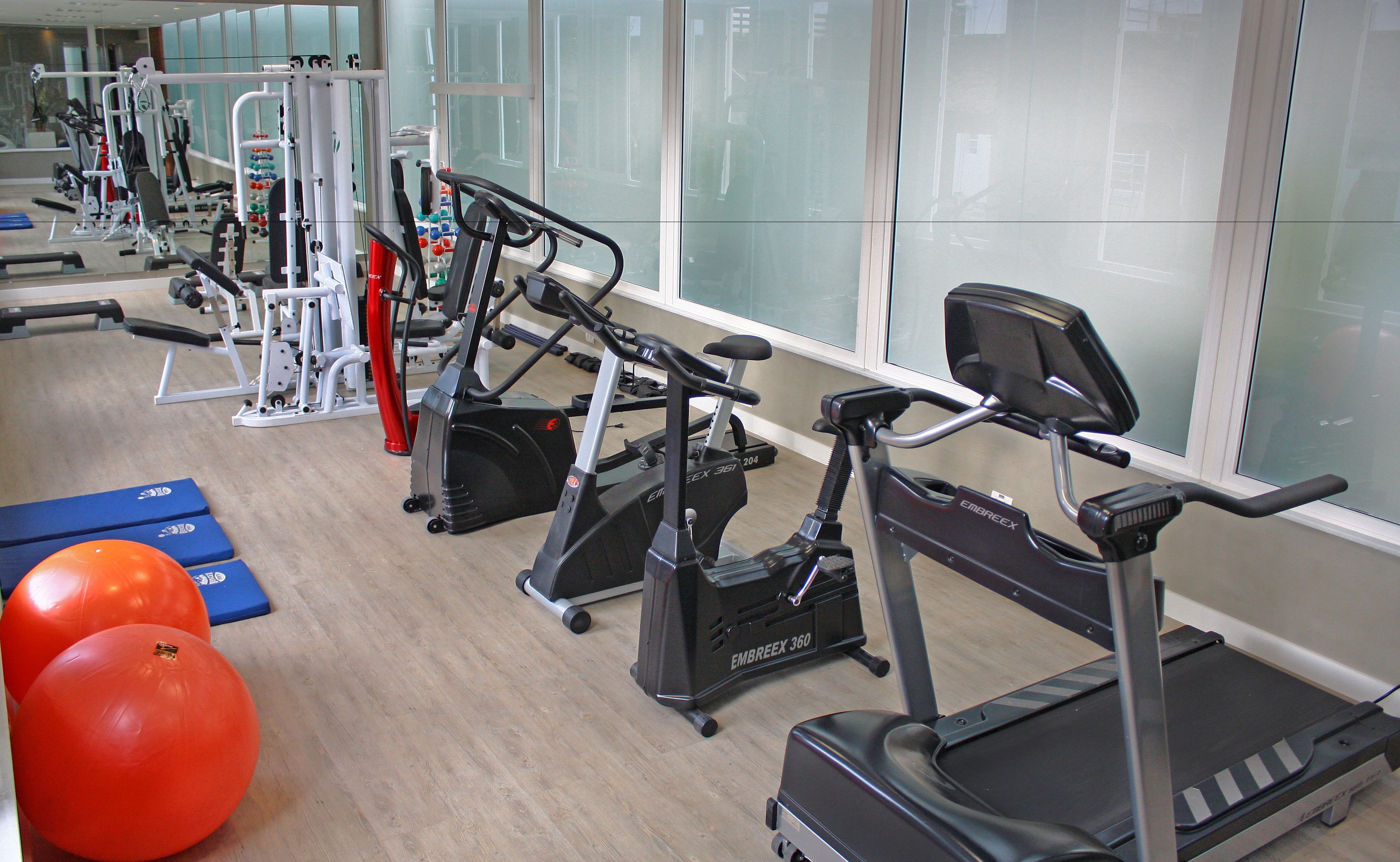 Ein Fitnessstudio mit verschiedenen Trainingsgeräten, darunter Laufbänder, Crosstrainer und Kurzhanteln.