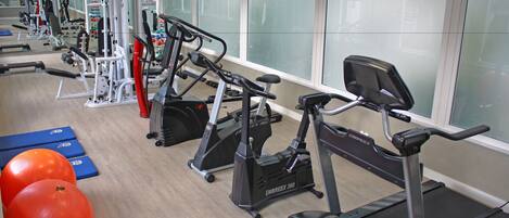 Ein Fitnessstudio mit verschiedenen Trainingsgeräten, darunter Laufbänder, Crosstrainer und Kurzhanteln.