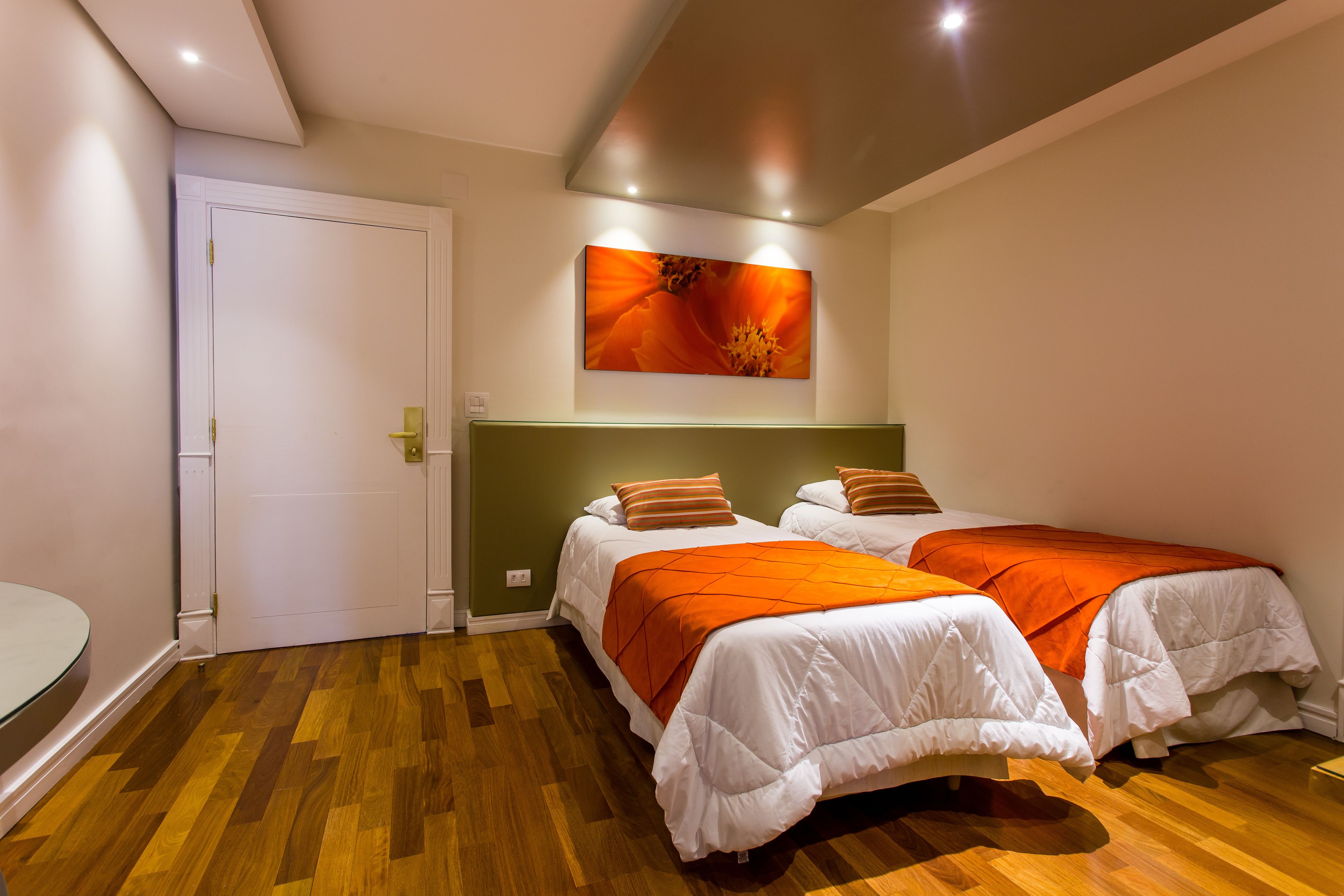 Una habitación de hotel con dos camas, una puerta blanca, un cuadro sobre las camas y suelo de madera.