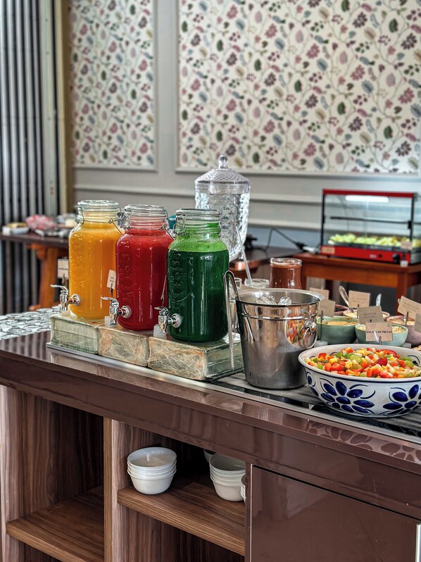 Una mesa de buffet con varios dispensadores de bebidas y un bol de frutas.