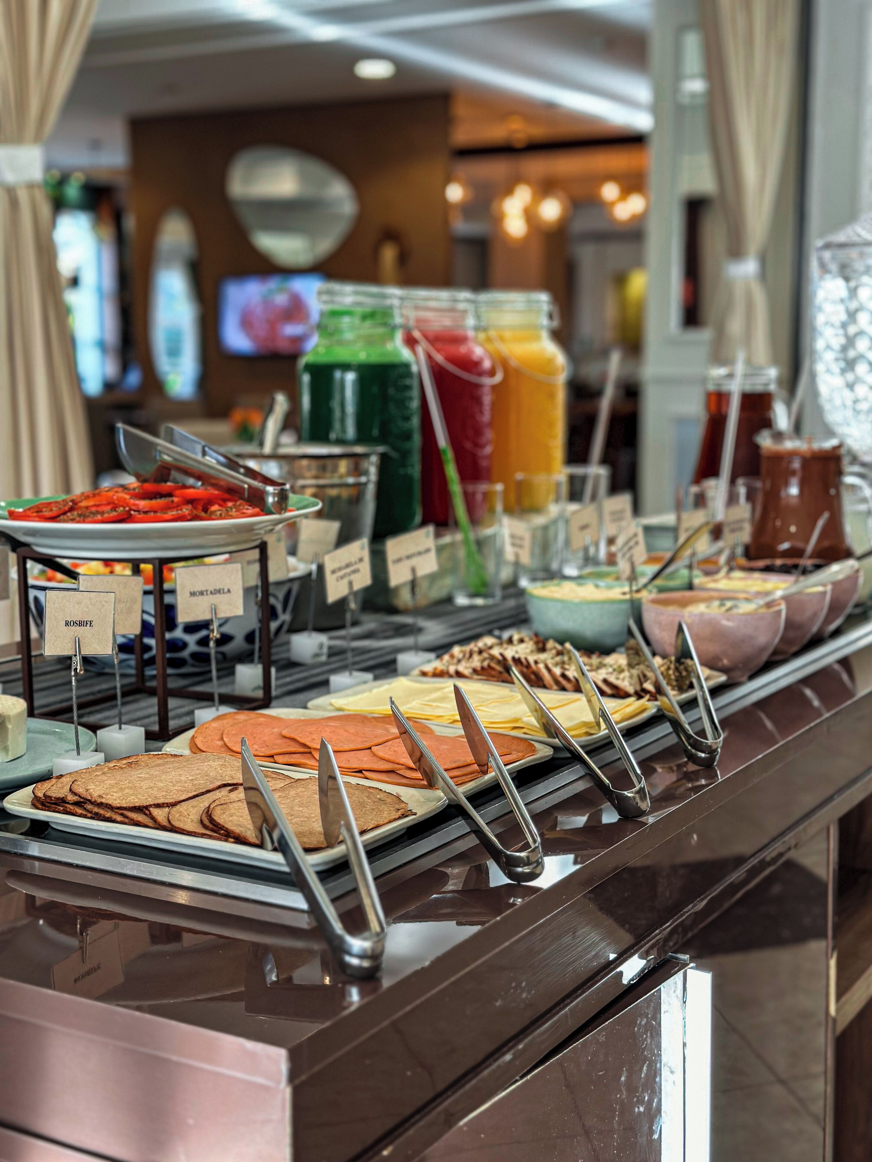 A buffet with various food items and beverages, including sliced meats, cheeses, and a selection of juices.