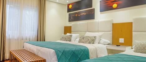 A hotel room with two beds, a wooden bench, and artwork on the wall.