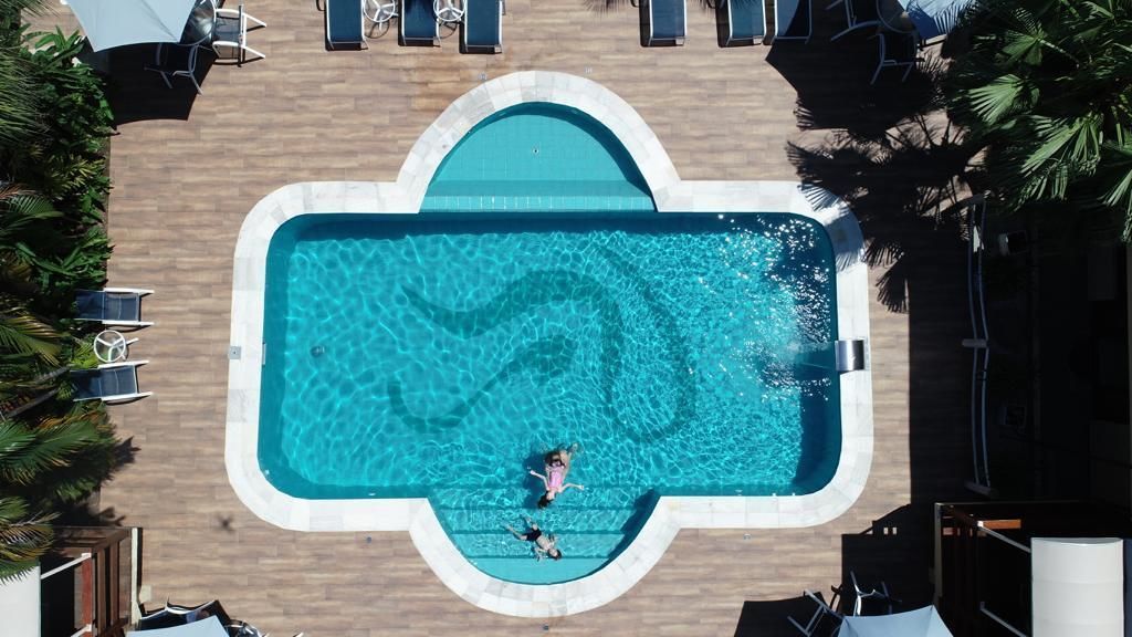 Vue aérienne d’une piscine à la forme originale, entourée de chaises longues et de palmiers.