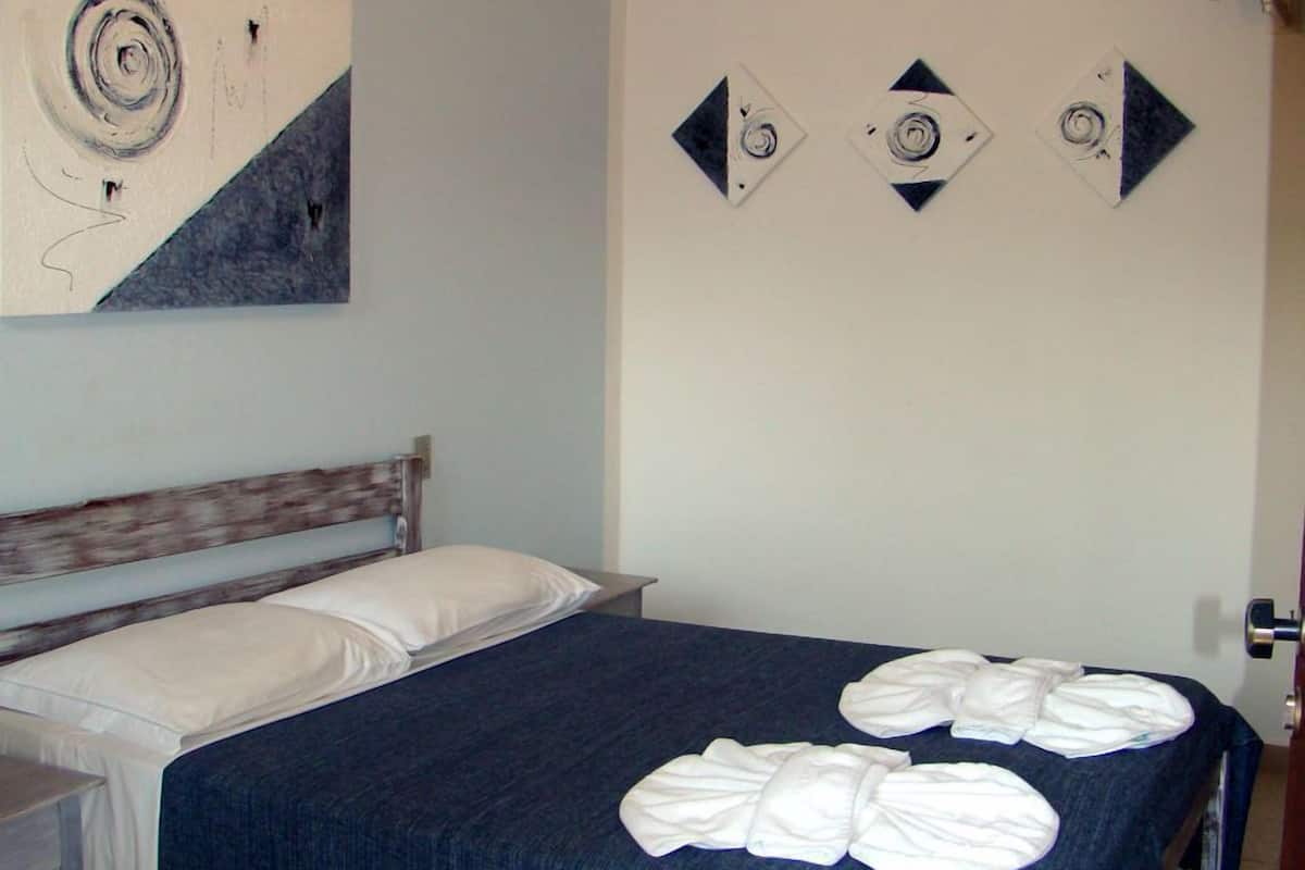Quarto com cama, mesa de cabeceira, ventoinha no teto e decoração nas paredes.