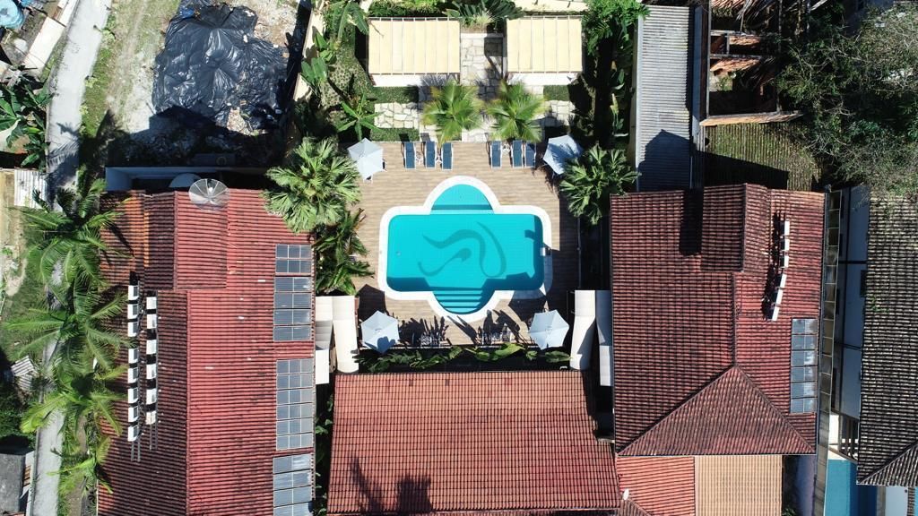 An aerial view of a hotel with a swimming pool, palm trees, and a red-roofed building.